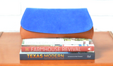 [Electric Blue Suede/Saddle Tan] Pommel Clutch front view sitting on stack of books