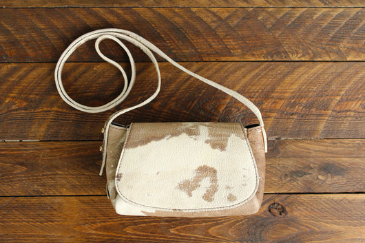 Cowhide Crossbody Saddle Bag front view features a unique pattern of shades of cream, khaki, and chocolate. Shown in color [Cowhide A].