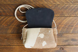 Cowhide Crossbody Saddle Bag open view features a unique pattern of shades of cream, khaki, and chocolate with an interior lining of Dark Denim Blue suede.. Shown in color [Cowhide A].