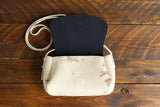Cowhide Crossbody Saddle Bag open view features a unique pattern of shades of cream, khaki, and chocolate and Dark Denim Blue suede interior. Shown in color [Cowhide B].