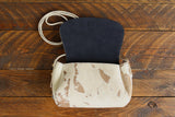 Cowhide Crossbody Saddle Bag open view features a unique pattern of shades of cream, khaki, and chocolate and Dark Denim Blue suede interior lining. Shown in color [Cowhide C].