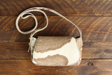 Cowhide Crossbody Saddle Bag front view features a unique pattern of shades of cream, khaki, and chocolate. Shown in color [Cowhide D].