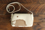 Cowhide Crossbody Saddle Bag front view features a unique pattern of shades of cream, khaki, and chocolate. Shown in color [Cowhide E].