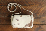 Cowhide Crossbody Saddle Bag front view features a unique pattern of shades of cream, khaki, and chocolate. Shown in color [Cowhide H].