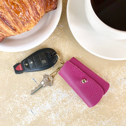 Fuchsia George Key Case on table next to coffee mug and croissant.